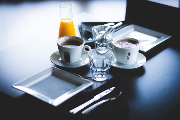 Un desayuno con un vaso de jugo de naranja, dos tazas de café, un vaso de agua y un plato.