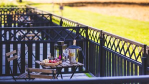 A wooden picnic table with a bottle of champagne, glasses, and a bowl of snacks on a deck with a black railing. - Domaine du Blé Hôtel (Wavre)