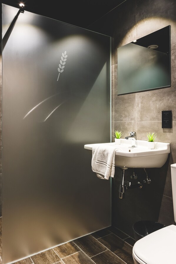 A modern bathroom with a large mirror, a sink, two potted plants, and a towel hanging on the sink. - Domaine du Blé Hôtel (Wavre)