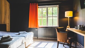 A hotel room with a bed, a desk with a lamp, and a window with curtains. - Domaine du Blé Hôtel (Wavre)