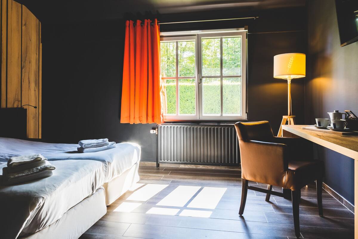 A hotel room with a bed, a desk with a lamp, and a window with curtains.