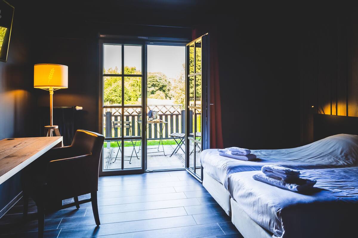 A hotel room with a bed, a desk, a chair, and a view of the outside.