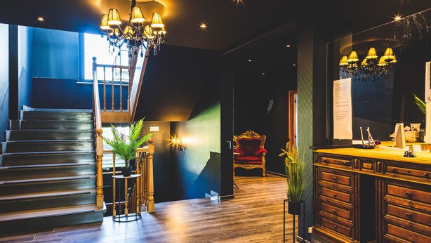 A modern hotel lobby with a staircase, a chandelier, a reception desk, and a red chair. - Domaine du Blé Hôtel (Wavre)