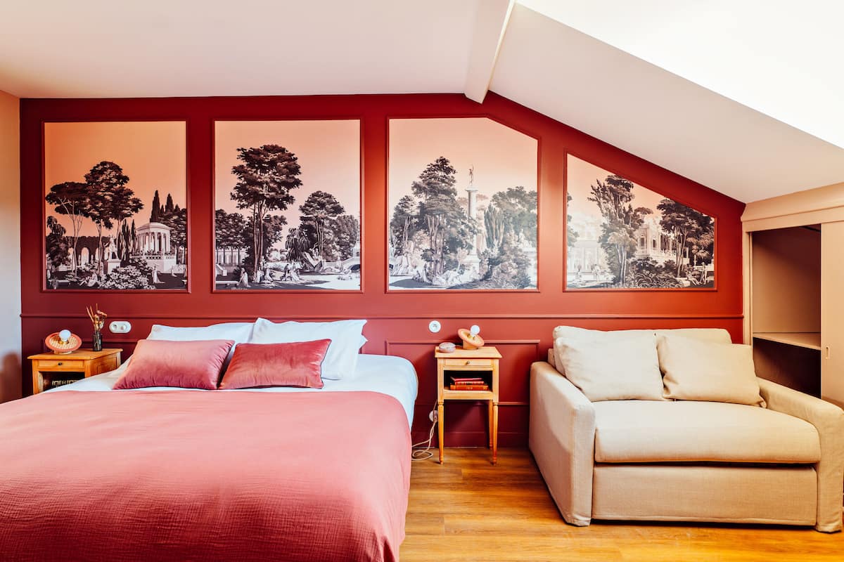 A bedroom with a bed, a sofa, and a nightstand with a lamp.