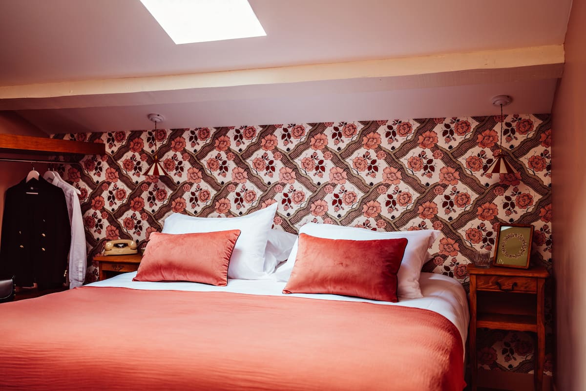 A bedroom with a bed, pillows, a nightstand, a telephone, and a wardrobe.