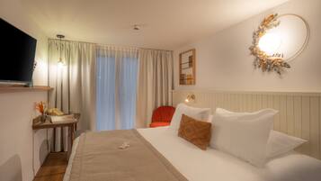 A hotel room with a bed, a desk with a telephone, a chair, a television, and a wall-mounted light fixture.