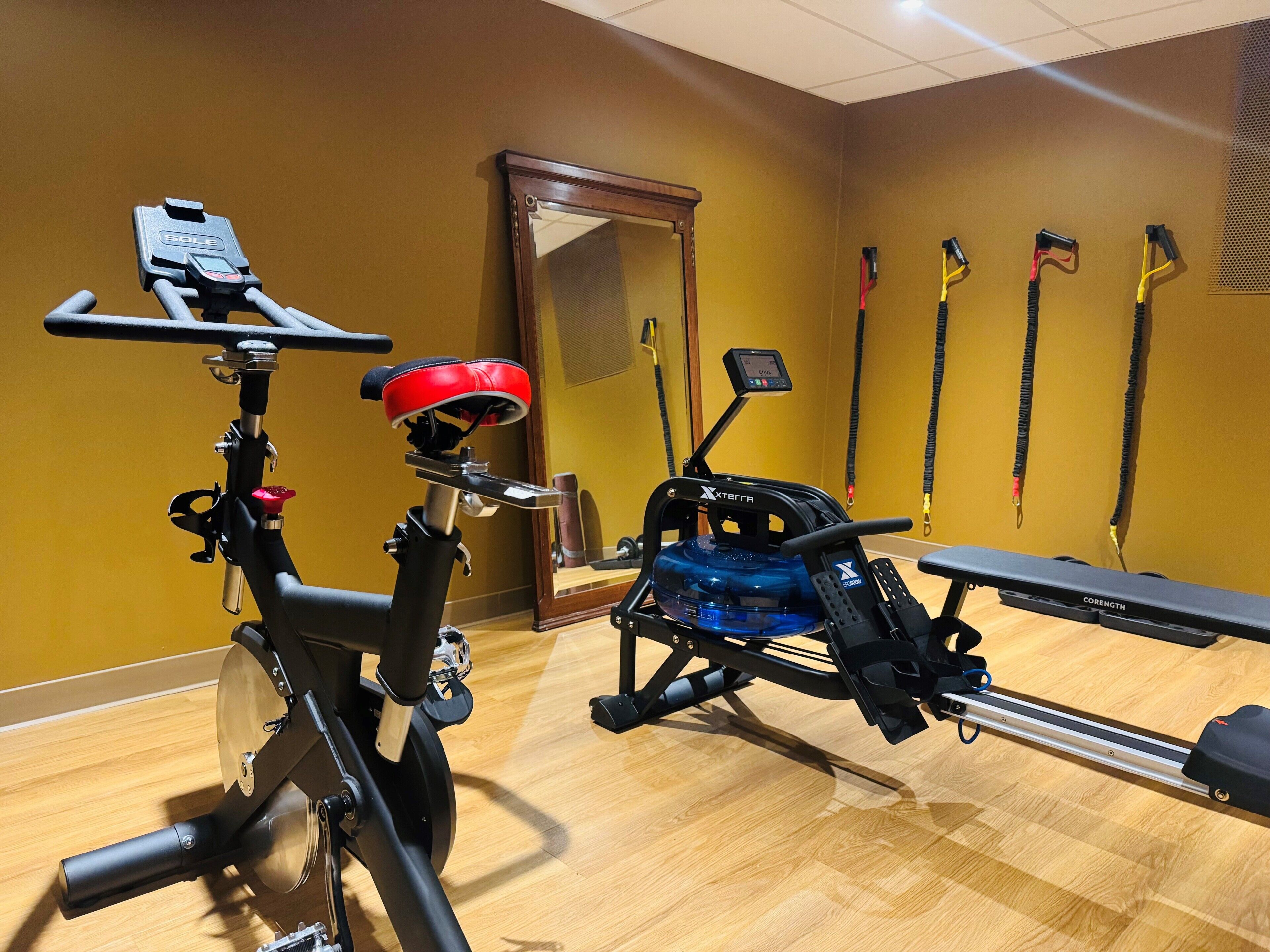A gym with stationary bikes, a rowing machine, and exercise equipment against a yellow wall.