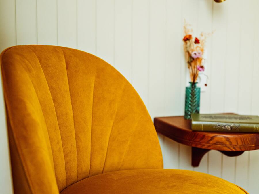 Een mosterdkleurige fauteuil met een gebogen rugleuning, voor een witte paneeldeur.
