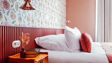 A bedroom with a wooden nightstand, a vase with dried flowers, a book, and a bed with white and red pillows.