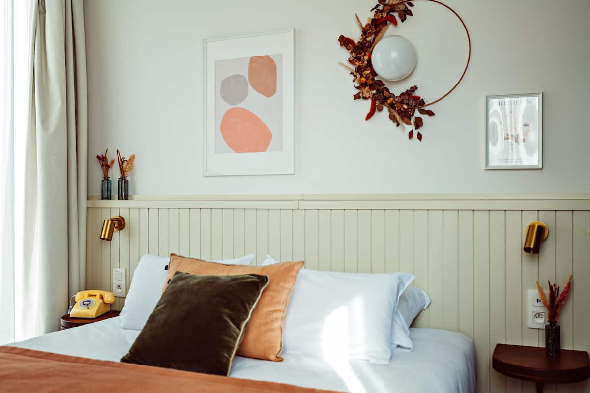 A neatly made bed with pillows, a bedside telephone, and a wall-mounted lamp.
