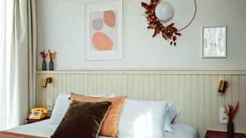 A neatly made bed with pillows, a bedside telephone, and a wall-mounted lamp.