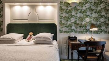 A neatly made bed with pillows, a teddy bear, and a desk with a lamp.