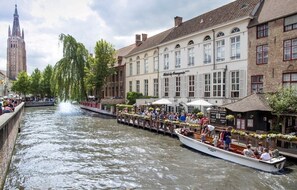 A canal-side boat tour with passengers, a historic building with 'Hotel de Bourgogne' signage, and a prominent tower in the background.