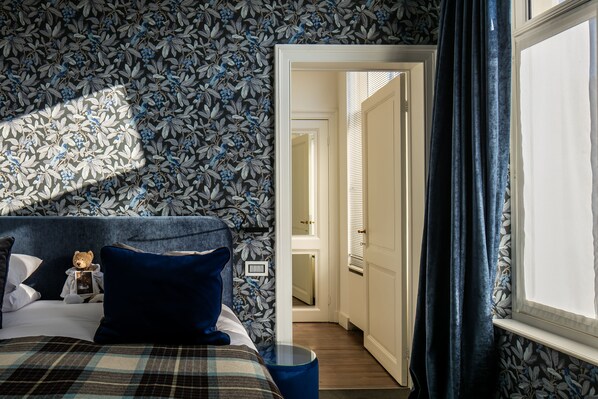 Cozy retreat with a plaid bedspread, nightstand, and leafy pattern wallpaper.