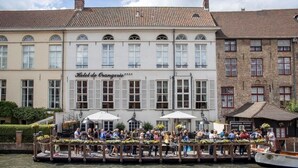 Un hotel con fachada clásica europea, un muelle con sombrillas y un cartel que indica un restaurante.