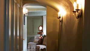 A hallway with a wooden floor, a bed with a white bedspread, and a nightstand with a lamp. - Hotel de Orangerie by CW Hotel Collection - Small Luxury Hotels of the World (Bruges)