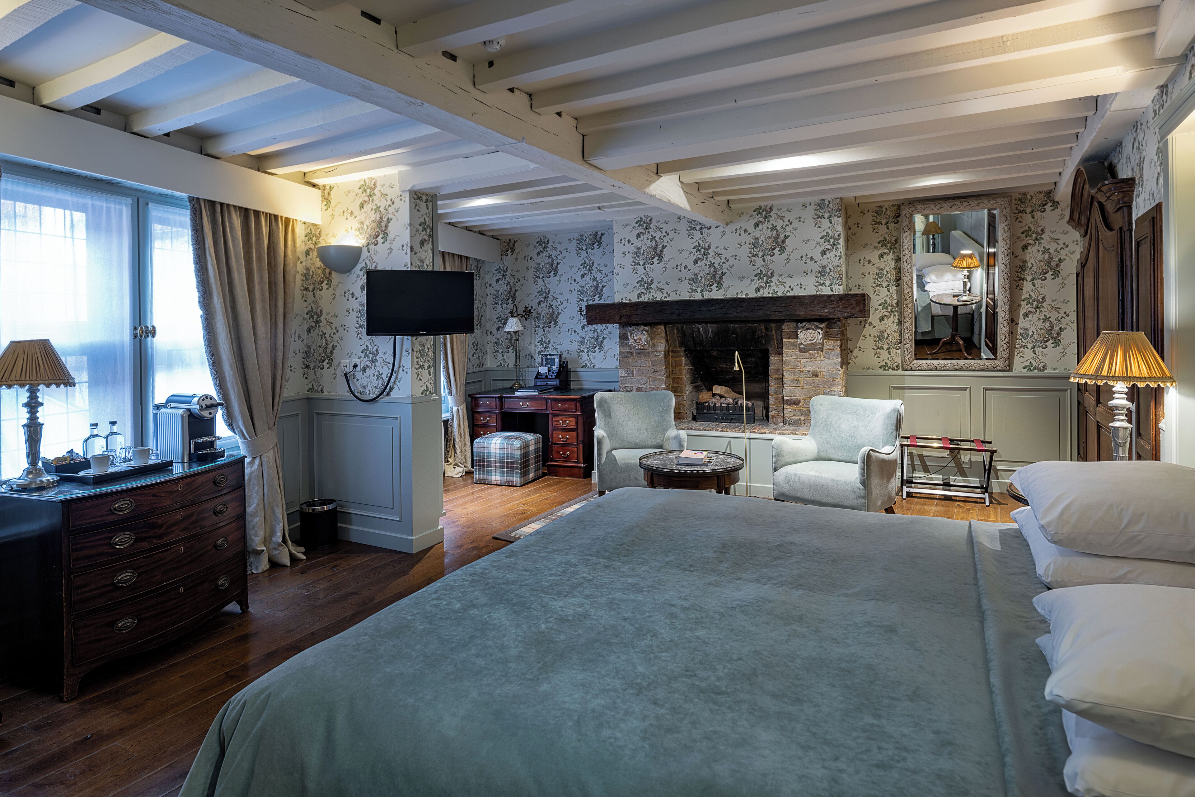 A hotel room with a large bed, a fireplace, a television, and a desk with a lamp.