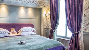 A hotel room with a large bed, a headboard with built-in lighting, a window with purple curtains, and a floral wallpaper pattern.