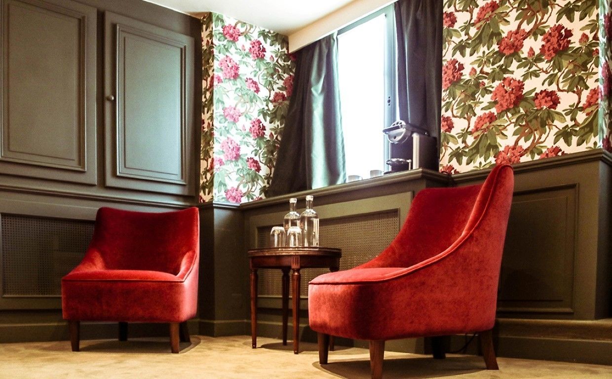 A room with two red velvet armchairs, a small wooden table, and floral wallpaper.