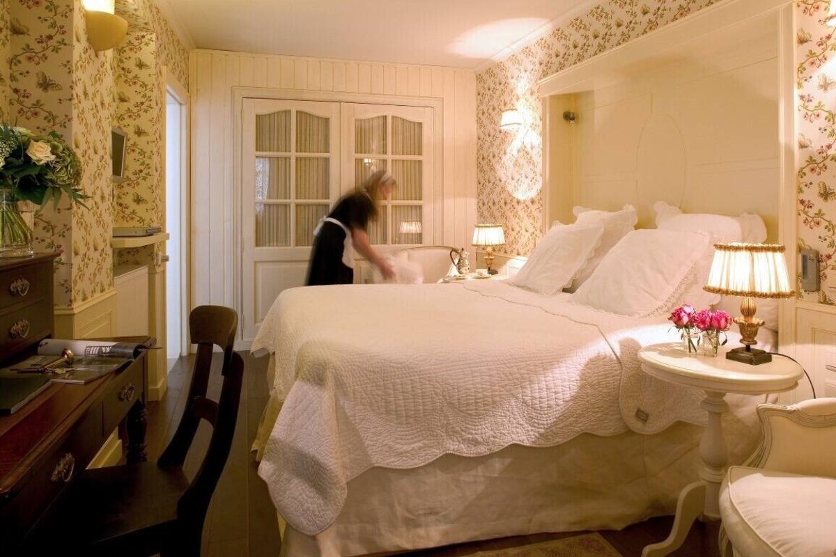 Quarto com cama grande, mesa de cabeceira com luminária, cômoda e cadeira.
