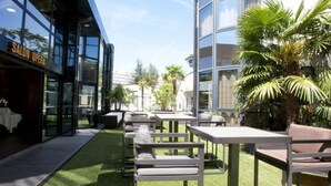 An outdoor seating area with tables and chairs, surrounded by palm trees and a building with a 'SALON OPERA' sign. - Palladia Hotel (Toulouse)