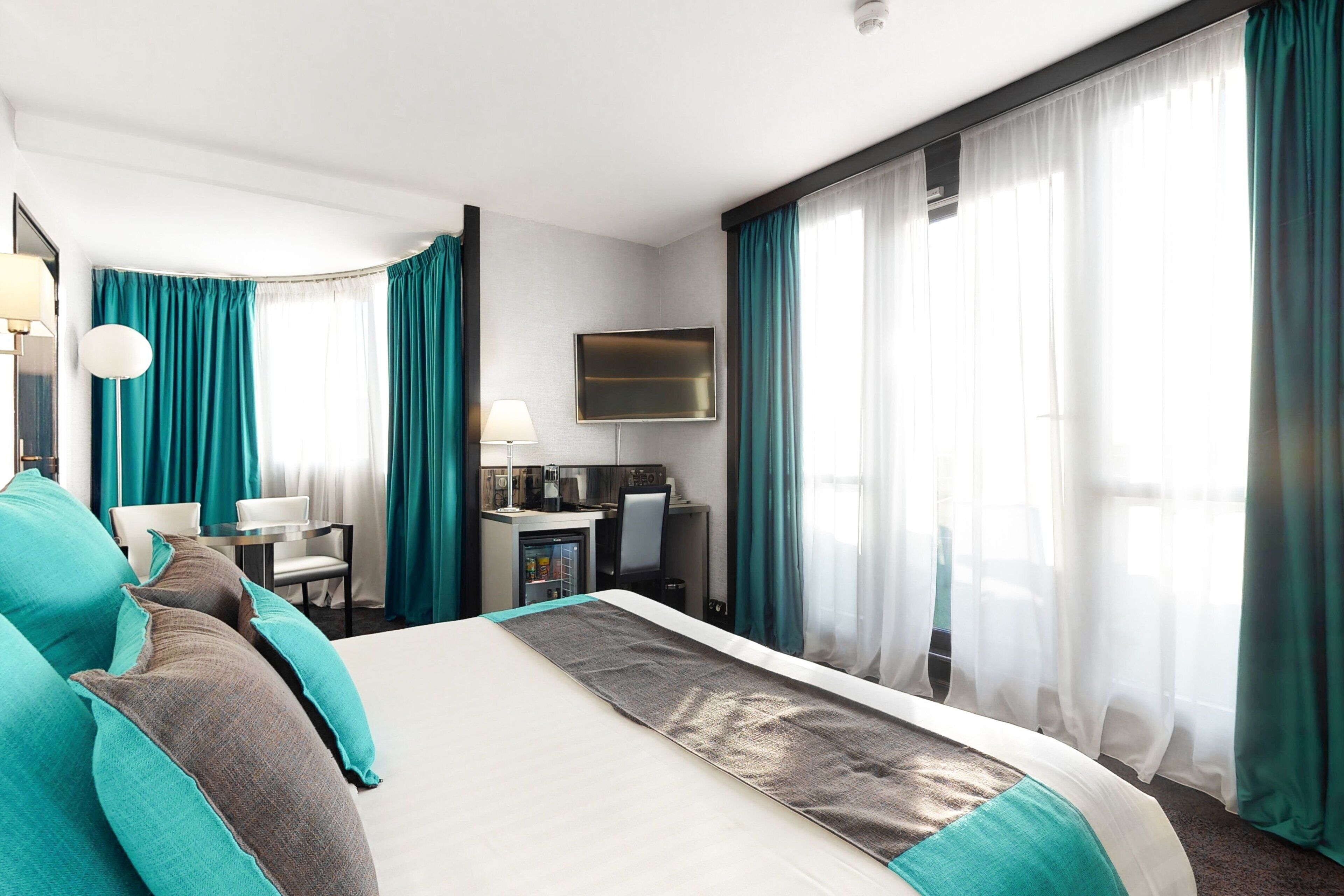 Habitación de hotel con una cama grande, un escritorio, una silla, un televisor y una kitchenette.