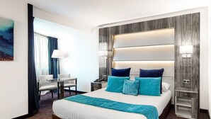 A hotel room with a large bed, two bedside tables, a desk with a chair, and a nightstand with a lamp. - Palladia Hotel (Toulouse)