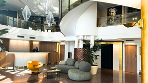 A modern hotel lobby with a reception desk, seating area, and a staircase leading to an upper level. - Palladia Hotel (Toulouse)