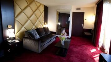 A hotel room with a tufted headboard, a dark sofa, a small table with a vase, and a red carpet.