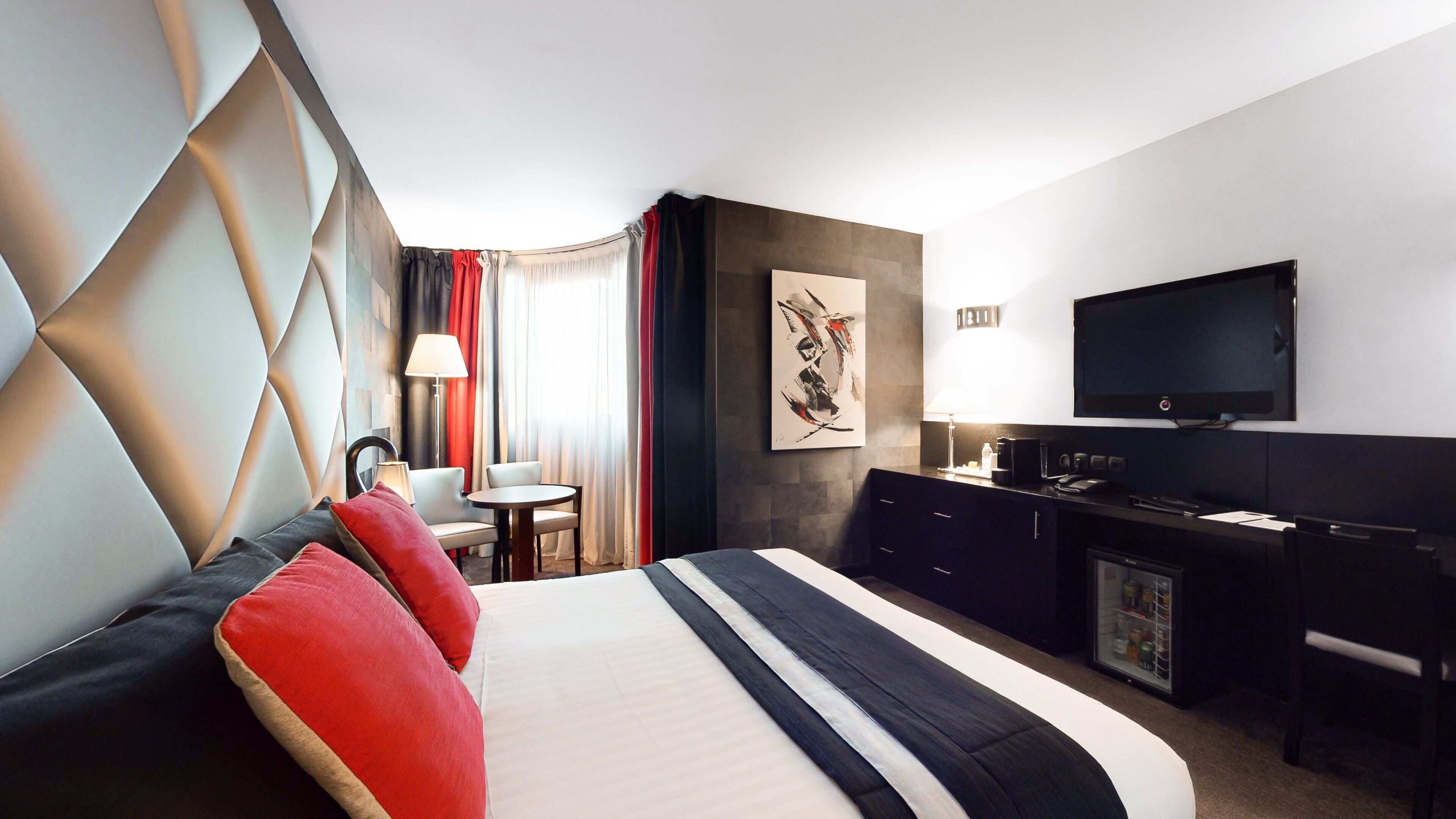 Una habitación de hotel con cama, escritorio, televisor y minibar.