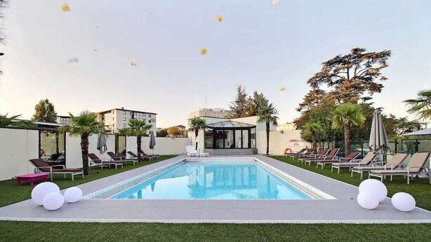 A swimming pool with lounge chairs and palm trees. - Palladia Hotel (Toulouse)