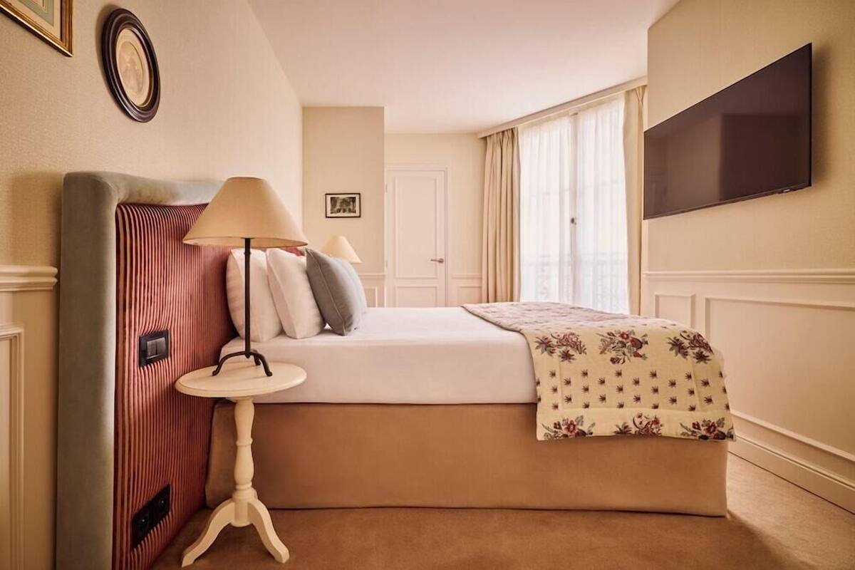 A hotel room with a bed, bedside table, lamp, TV, and a door.