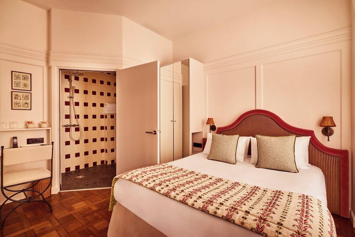 A hotel room with a large bed, a desk, a shower area, and a door leading to another room.