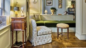 A room with a herringbone wooden floor, a green sofa, a patterned armchair, and a small wooden table with a lamp. - Hôtel Maison Monceau (Paris)