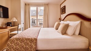 A hotel room with a bed, a desk, a chair, a television, and a window with curtains. - Hôtel Maison Monceau (Paris)