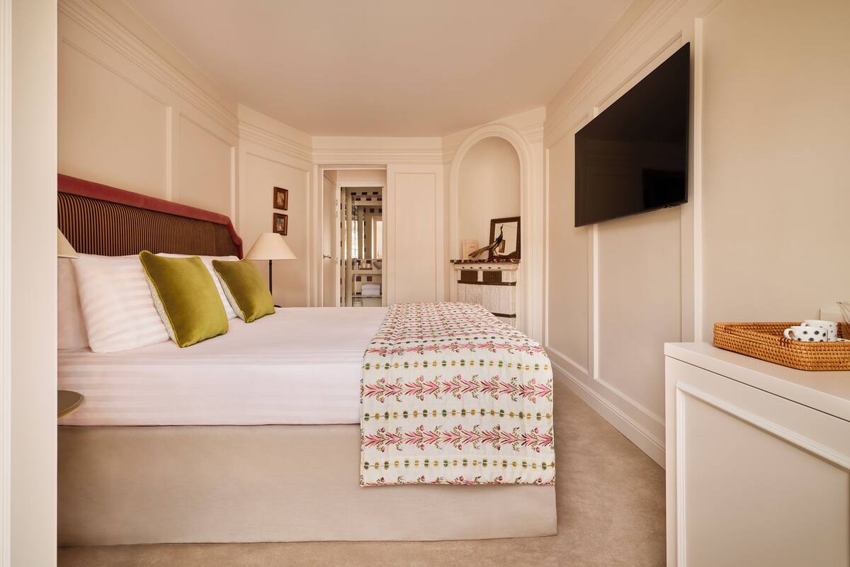 A hotel room with a large bed, a television, and a small table with a basket.