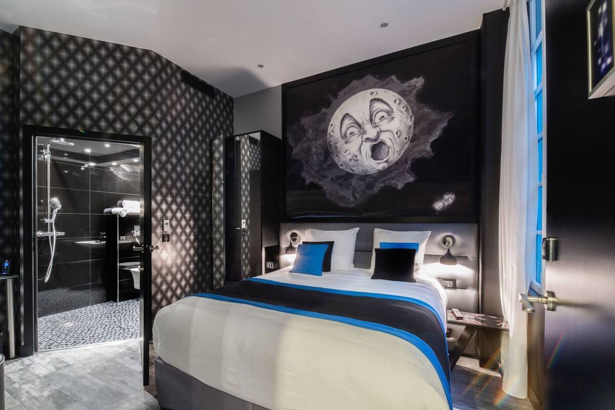 A modern bedroom with a large bed, a glass-enclosed shower, and a wall mural.