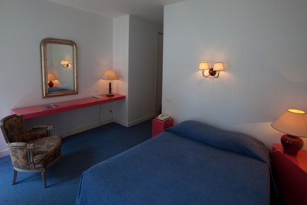 Una habitación de hotel con una cama, un escritorio, una silla, un espejo y dos lámparas de pared.