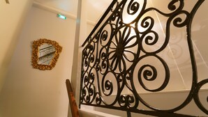 A staircase with a decorative metal railing and a wall-mounted mirror with an ornate frame. - Hostel Toulouse Wilson (Toulouse)