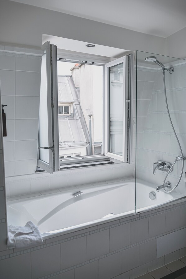 A modern bathroom with a glass shower enclosure, a bathtub, and a window overlooking a residential area.