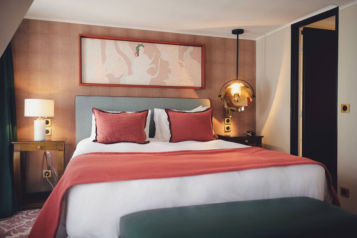 Habitación de hotel con una cama grande, una mesita de noche con lámpara, una obra de arte en la pared y una puerta.
