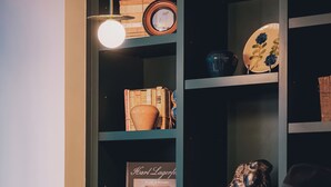 Una mujer sentada en un sofá rojo en una habitación con un armario verde oscuro, sosteniendo un vaso de agua.