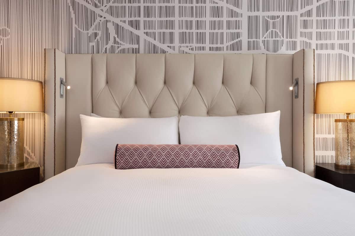A hotel room with a tufted headboard, white bedding, and patterned throw pillows.