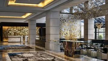 A modern hotel lobby with a marble floor, a reception desk, and a staircase.