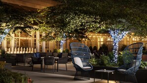 An outdoor seating area with wicker chairs and tables, surrounded by greenery and string lights. - Fairmont Washington, D.C., Georgetown (Washington)