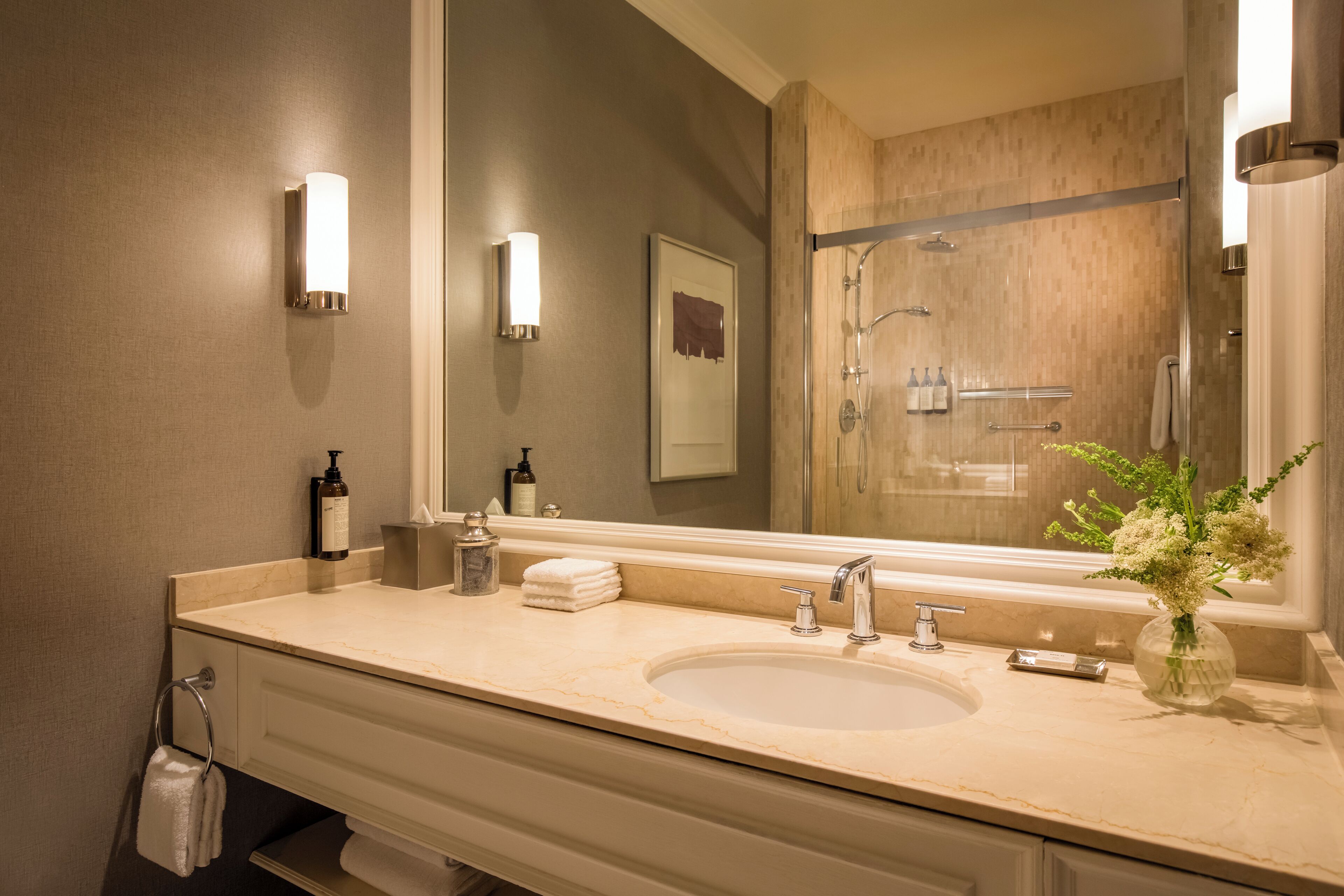 Un baño con un espejo grande, un lavabo, una ducha y un florero con flores.