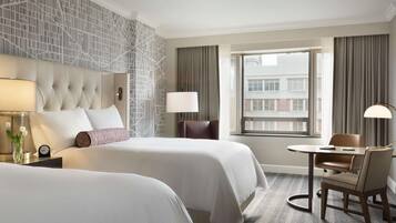 A hotel room with two beds, a sitting area with a table and chairs, a large window with curtains, and a patterned wall.