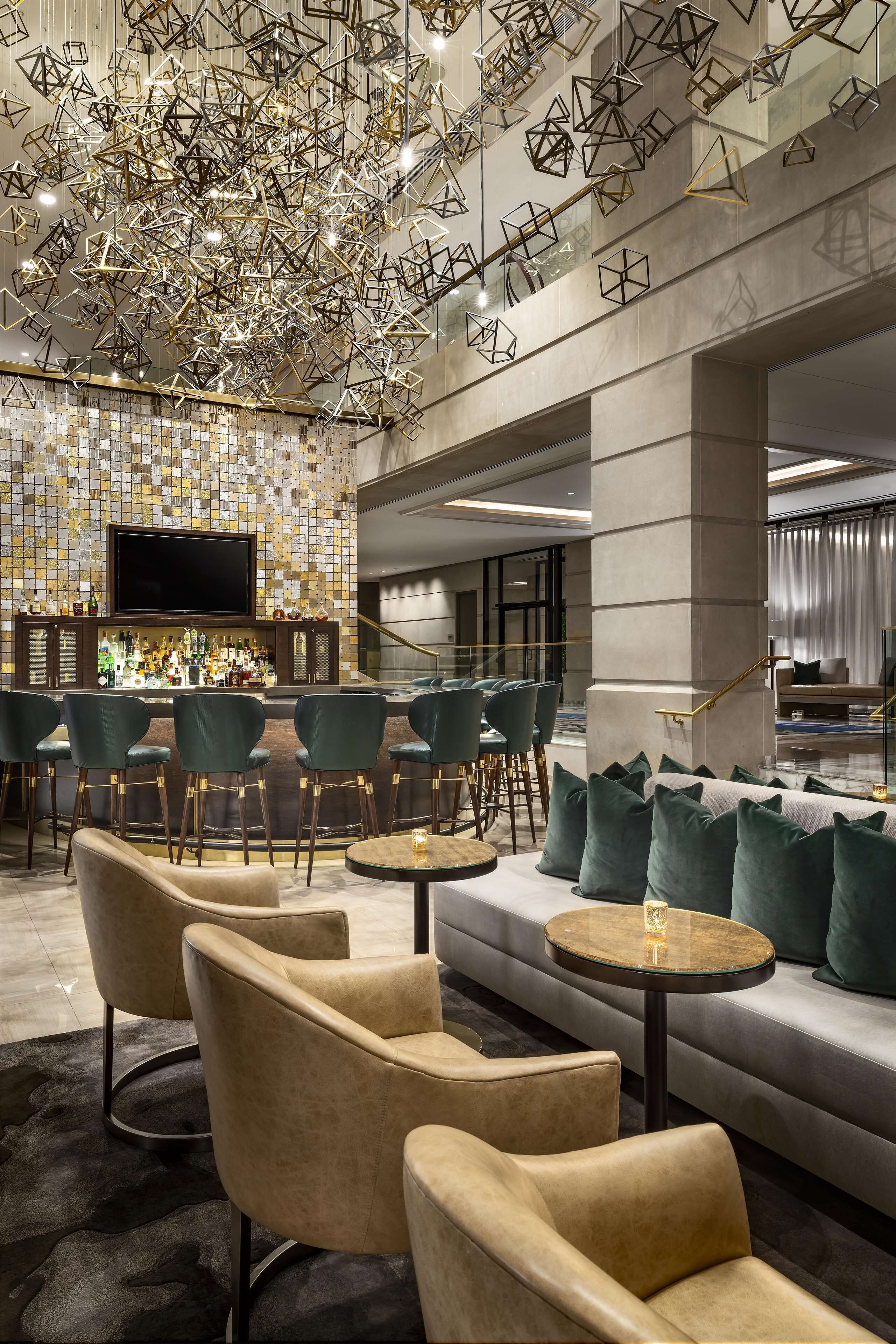 A modern bar area with a mosaic wall, multiple seating options including sofas and chairs, and a large flat-screen TV.