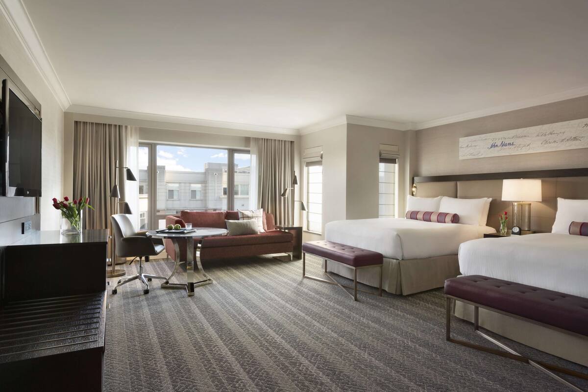 A hotel room with a large bed, a desk with a computer, a sofa, and a dining table.
