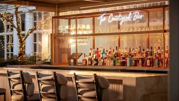 Un bar con un letrero de neón que dice "The Courtyard Bar", con una variedad de botellas de licor y un área de estar con sillas.